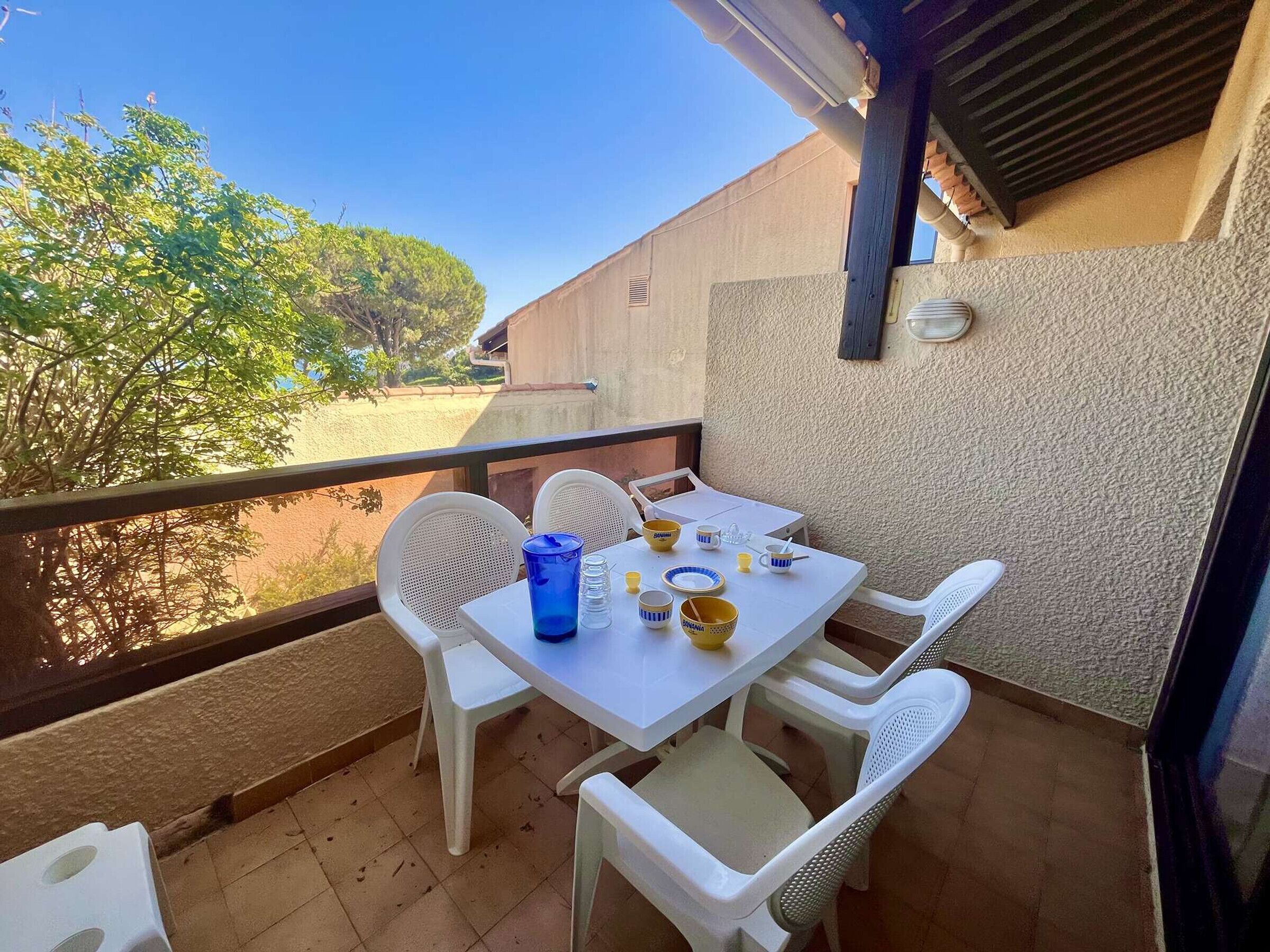 A balcony with a table set for two, white plastic chairs, and a blue water bottle.