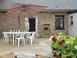 Un patio al aire libre con un edificio de piedra, sillas de plástico blanco, una mesa y un paraguas grande.