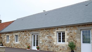 Un edificio de piedra con techo gris, dos ventanas y una puerta.