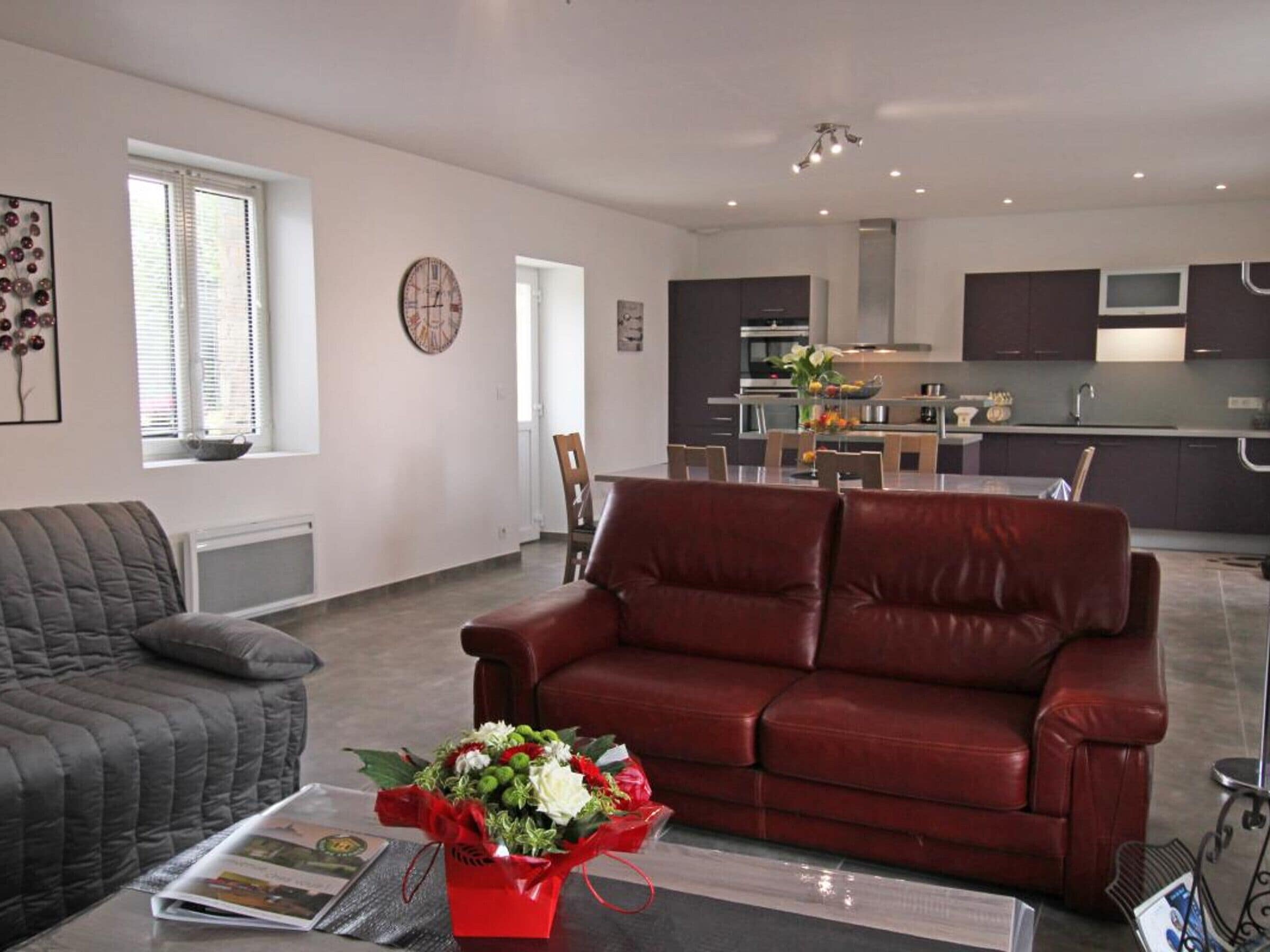 Una sala de estar moderna con un sofá de cuero rojo, un sillón gris y una mesita de centro con una revista y un ramo de flores.