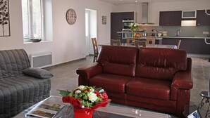 Una sala de estar moderna con un sofá de cuero rojo, un sillón gris y una mesita de centro con una revista y un ramo de flores.