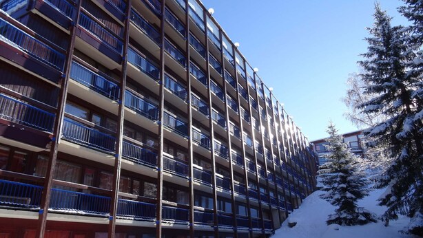 A multi-story hotel with balconies, a snow-covered slope, and a snow-laden tree. - Charming studio for 4, chalet style, pets allowed (Les Arcs 1800)