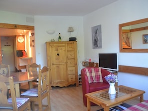 A cozy living room with a wooden cabinet, a red sofa, a glass coffee table, and a television. - Charming studio for 4, chalet style, pets allowed (Les Arcs 1800)