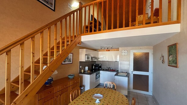 A kitchen with a dining table, wooden staircase, and a small dining area. - 2-Bedroom Apartment - 50m from the beach, parking (Les Sables-d'Olonne)