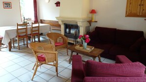 Een gezellige woonkamer met een open haard, een eethoek met een tafel en stoelen, en een bank.