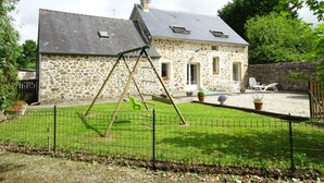 Een stenen huis met een schuin dak, een schommel en een omheind terras.