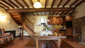 A spacious living area with a wooden staircase, a dining table with benches, and a kitchen with wooden cabinets and a stone wall. - Comfortable house in the heart of the Norman bocage with garden and pets allowed (Doville)