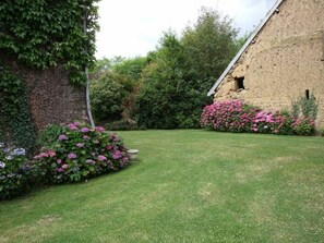 Um jardim com um edifício de pedra, vegetação exuberante e plantas floridas.
