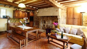 A rustic kitchen with wooden beams, a stone fireplace, and a dining area with a wooden table and benches. - Comfortable house in the heart of the Norman bocage with garden and pets allowed (Doville)