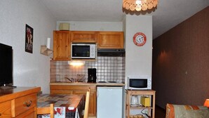A compact kitchen with wooden cabinets, a microwave, a coffee maker, and a small refrigerator.