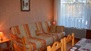A cozy room with a sofa, a table with a patterned tablecloth, and a window with a view of trees.