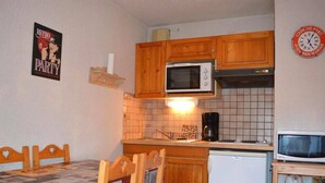 A compact kitchen with wooden cabinets, a microwave, a coffee maker, and a refrigerator.