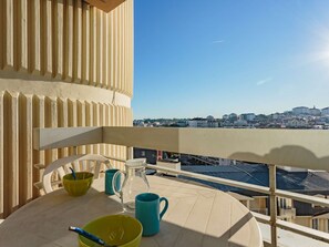 Een balkon met een tafel gedekt voor twee personen, een helder uitzicht op de stad en een gebouw met verticale beplating.
