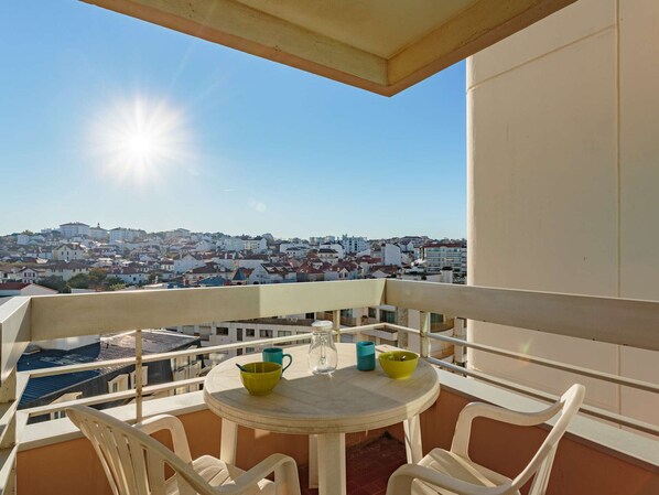 Een balkon met een tafel en stoelen, met uitzicht op een stadsgezicht.