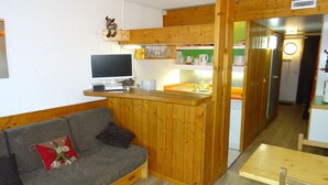 Ett kompakt vardagsrum med ett litet kök med träinredning, en grå soffa och ett litet matbord.