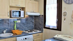 Una cocina con lavavajillas Bosch, microondas, estufa y un fregadero. Hay una ventana con cortinas y un reloj de pared.