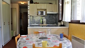 Cocina compacta con microondas, estufa y fregadero. En primer plano, una mesa de comedor con sillas.