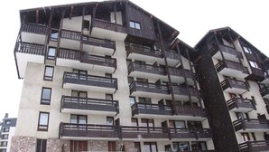 Un edificio de varios pisos con balcones, base de piedra y suelo cubierto de nieve.