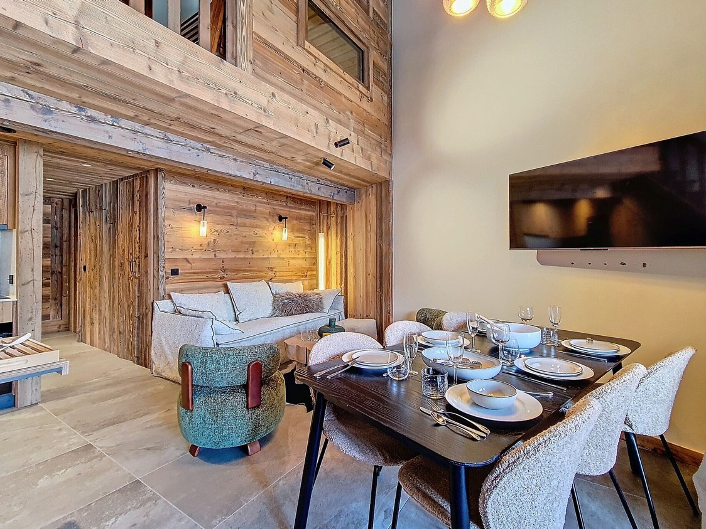 Een eethoek met een houten tafel voor vier personen, een bank en een aan de muur bevestigde televisie.