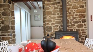 A stone-walled room with a fireplace, a table with a tray of items, and a clock on the wall. - Charming cottage with Internet near Mont Saint-Michel (Les Chambres-Le Grippon)