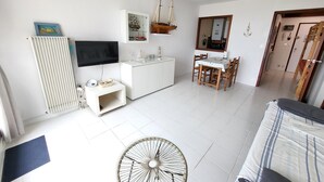 A living room with a TV, white cabinets, a dining table, and a ceiling fan.