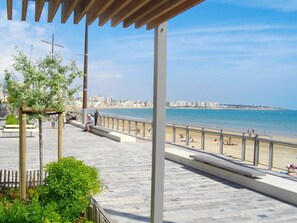 A coastal promenade with a wooden deck, benches, and a view of the beach and city skyline.