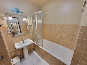 A bathroom with a sink, mirror, shower enclosure, and patterned tiles.