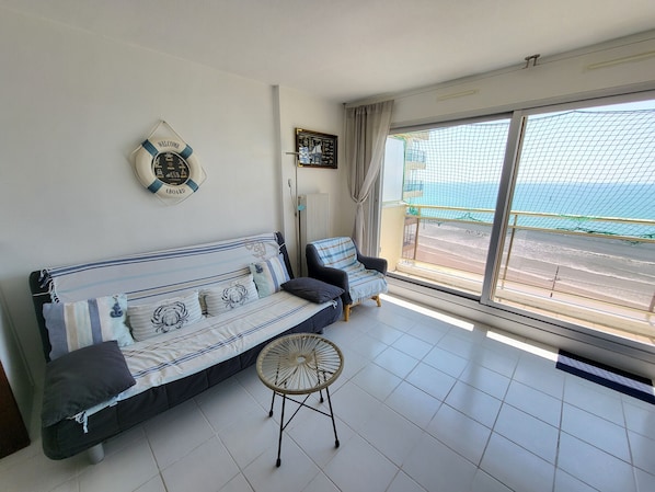 Una habitación con sofá, una mesita redonda pequeña, un letrero que dice 'WELCOME ABOARD', vistas al mar a través de un ventanal grande y un balcón con barandilla.