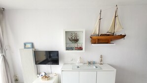 A room with a white TV, a small table with a remote, a white cabinet, and two model ships on the wall.