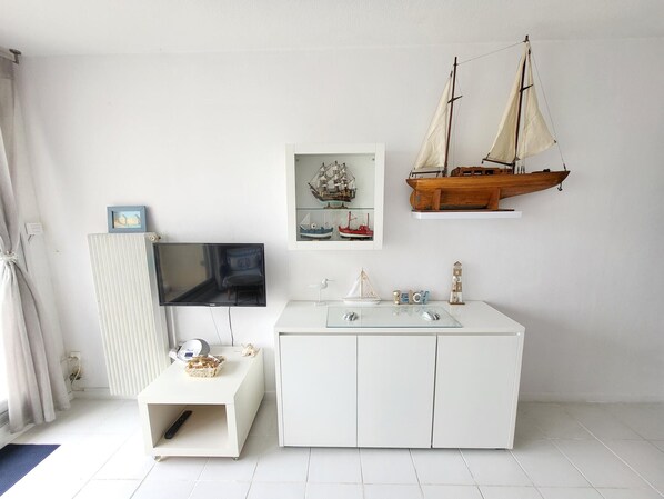 A room with a white TV, a small table with a remote, a white cabinet, and two model ships on the wall.