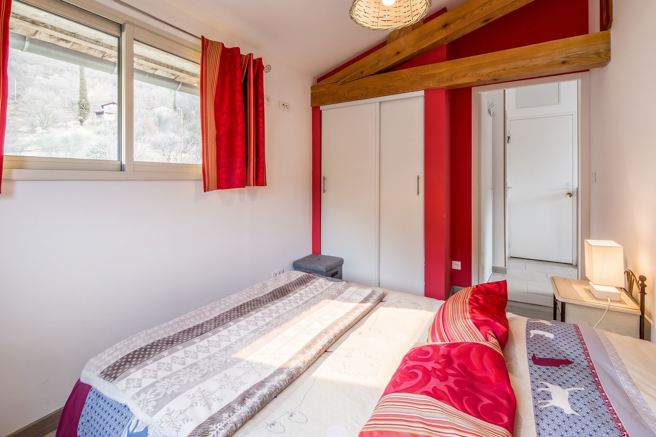 Une chambre à coucher avec un lit, une table de chevet avec une lampe, une fenêtre avec des rideaux et une armoire.