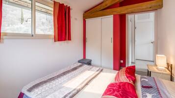 Une chambre à coucher avec un lit, une table de chevet avec une lampe, une fenêtre avec des rideaux et une armoire.