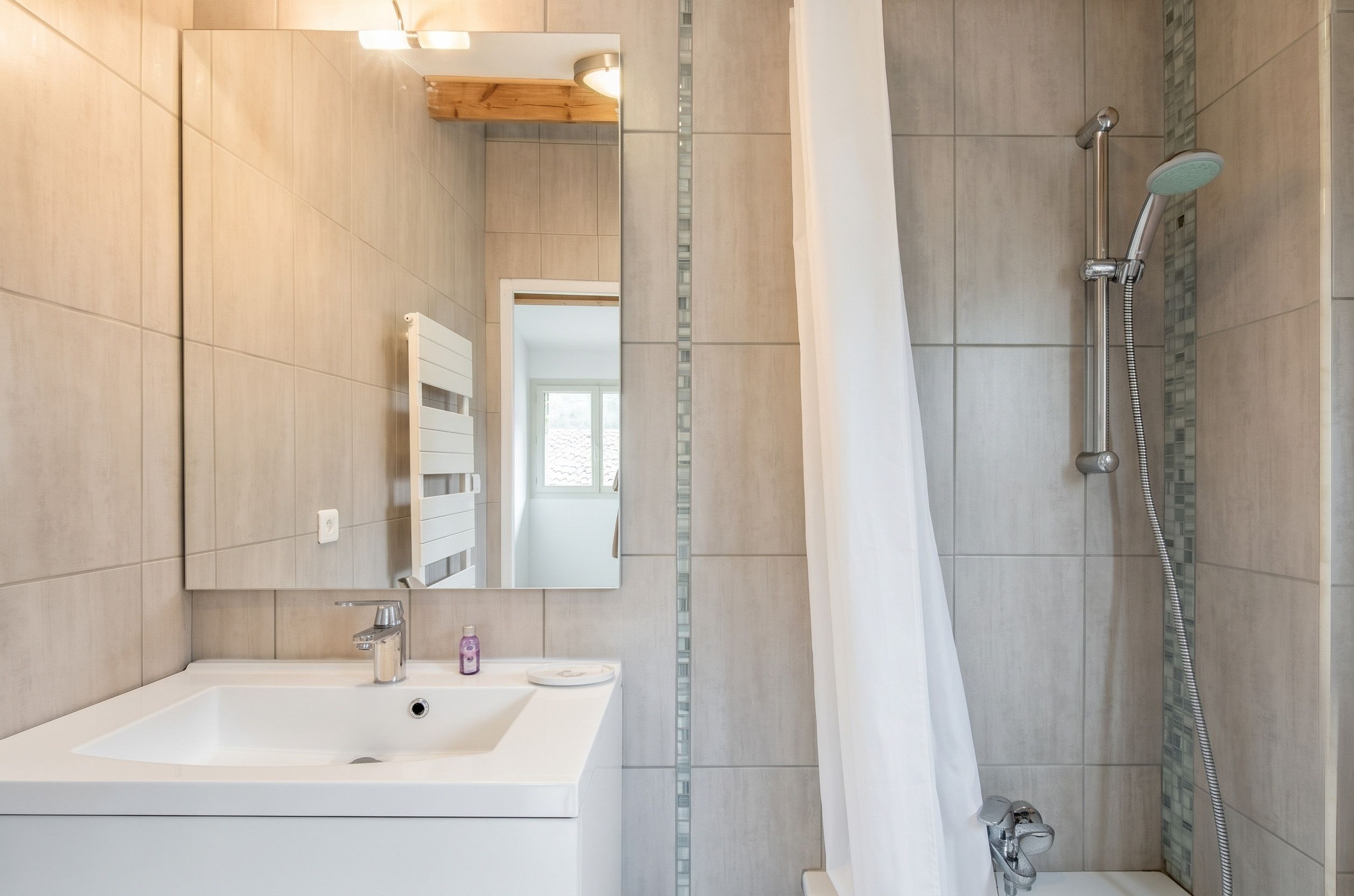 Ein modernes Badezimmer mit einem weißen Waschbecken, einem Spiegel und einer Duschkabine mit Glastür.