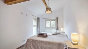 Une chambre à coucher comprenant un lit, une table de chevet, une lampe, une fenêtre et des poutres en bois au plafond.