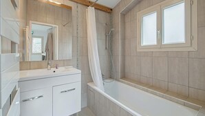 Une salle de bain moderne équipée d’une baignoire, d’une douche, d’un meuble-lavabo avec un miroir et d’une fenêtre en verre dépoli.