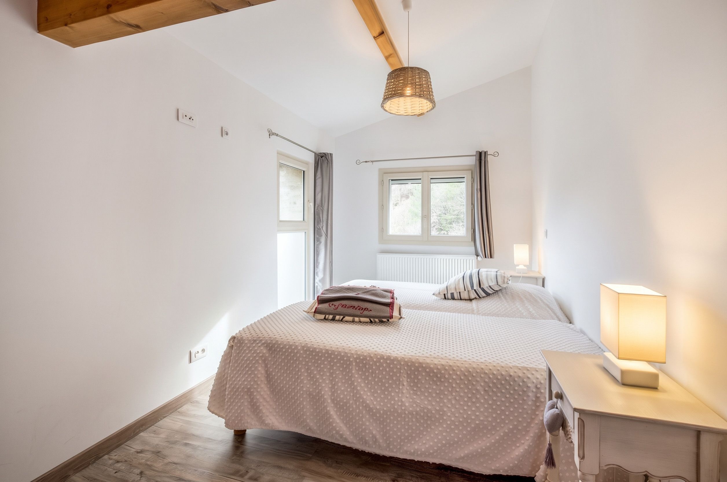 Une chambre à coucher avec un lit, une table de chevet, une lampe, une fenêtre et un luminaire au plafond.