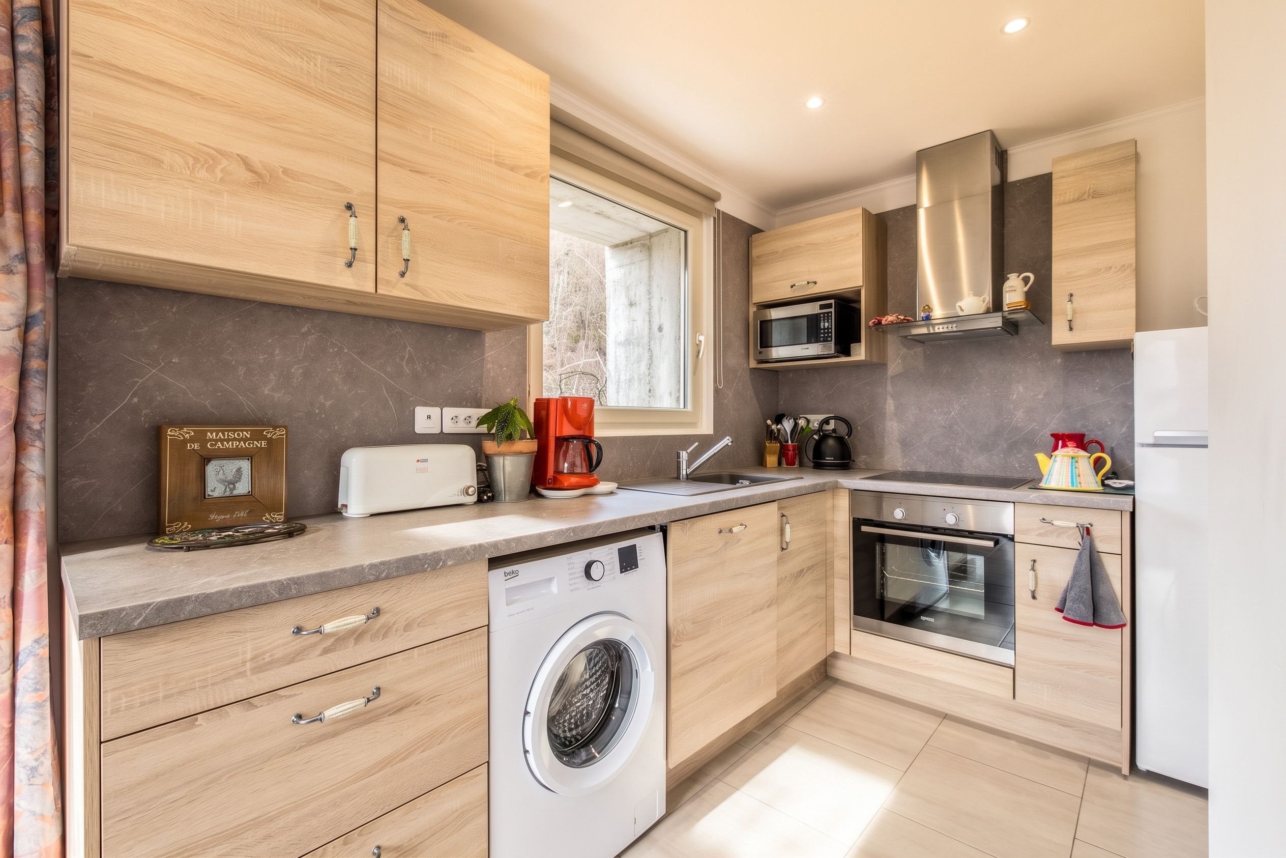 Een moderne keuken met houten kastjes, een ingebouwde wasmachine, een magnetron en een roestvrijstalen oven.