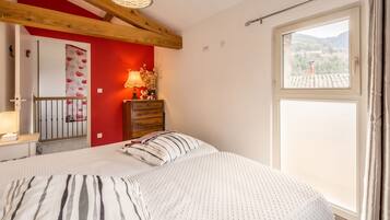 Une chambre à coucher comprenant un lit, une commode, une table de chevet, une lampe et une fenêtre donnant sur l’extérieur.