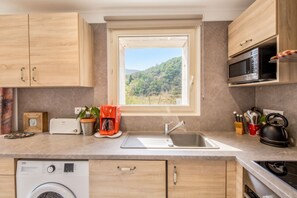 Eine moderne Küche mit Holzausstattung, einer eingebauten Mikrowelle, einer Kaffeemaschine und Blick auf eine Berglandschaft durch ein Fenster.