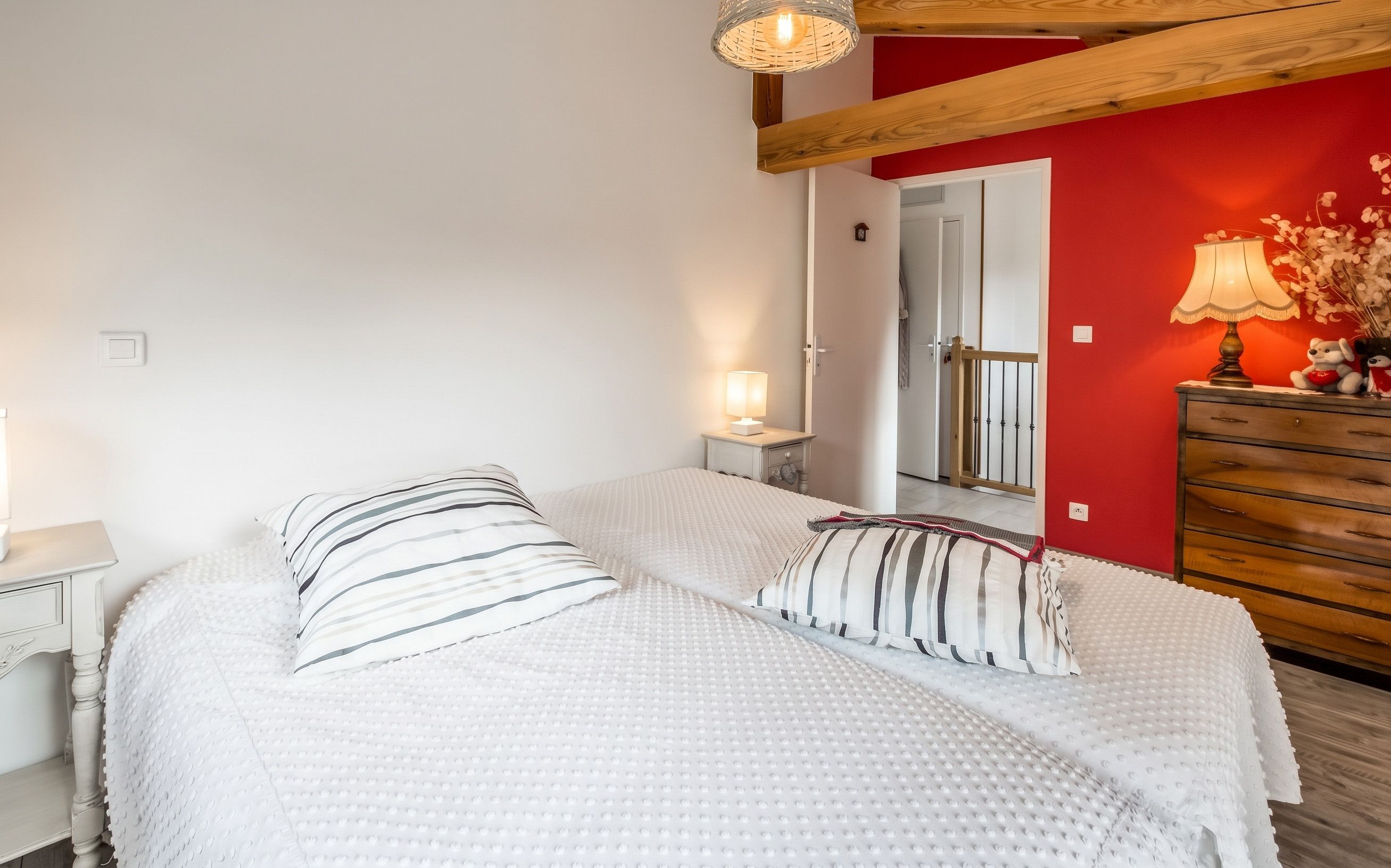 Een slaapkamer met twee bedden, een kaptafel, een lamp en een rode accentmuur.