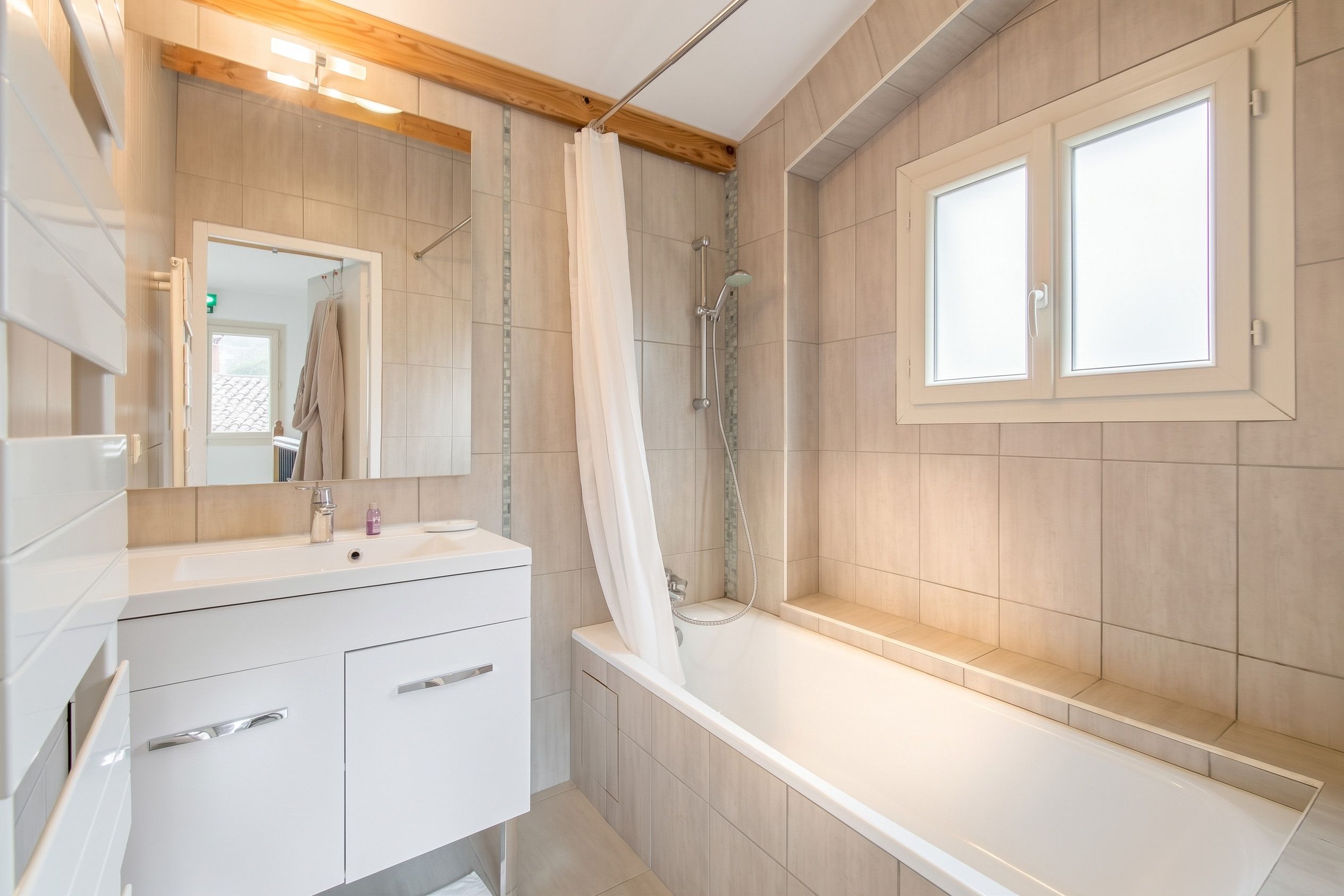 Een moderne badkamer met een badkuip, douche, een wastafel met lades en een grote spiegel.