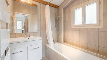 Een moderne badkamer met een badkuip, douche, een wastafel met lades en een grote spiegel.