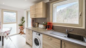 Une cuisine moderne équipée d’un lave-linge, d’un évier et d’une grande fenêtre donnant sur un paysage montagneux.