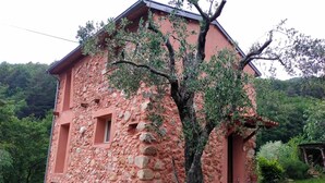 Un bâtiment rustique en pierre, doté d’un toit en pente, d’une petite fenêtre et d’un arbre devant.
