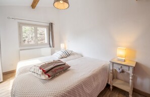 Un dormitorio con una cama grande, una mesita de noche con lámpara, una ventana con cortinas y un radiador.
