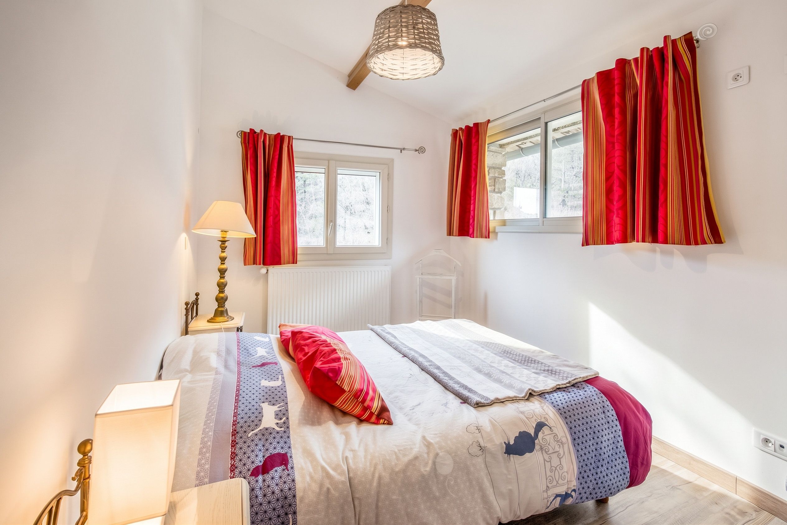 Ein Schlafzimmer mit einem Bett, einem Nachttisch mit Lampe, einem Fenster mit Vorhängen und einer Heizung.