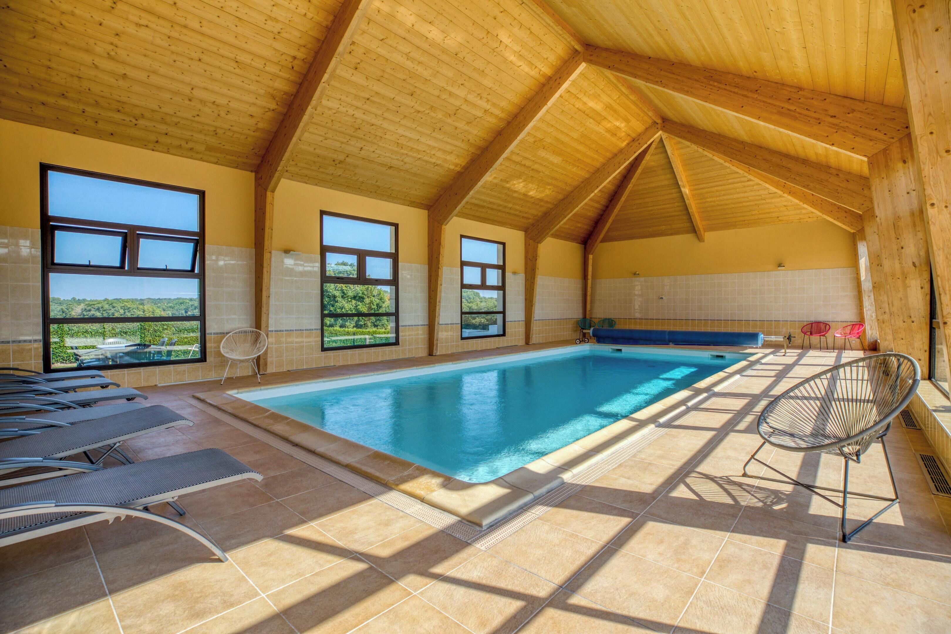 En indendørs swimmingpool med klare udsigter gennem store vinduer, trælofter og solbelyste fliser.