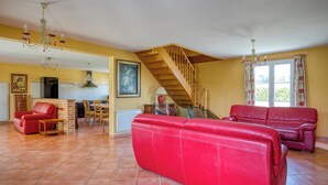 A spacious living area with a red sofa, a dining table, and a staircase leading to an upper floor.