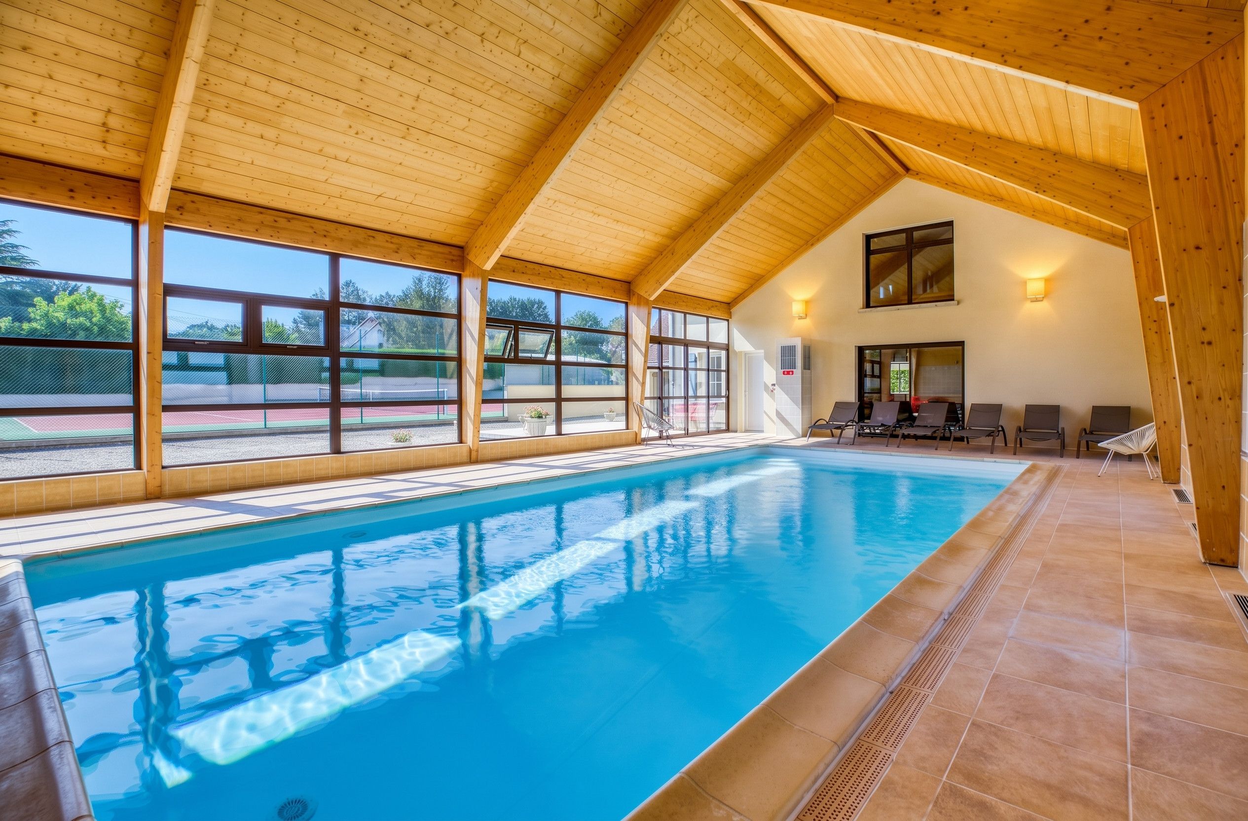 A swimming pool with a wooden ceiling and large windows.