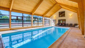 A swimming pool with a wooden ceiling and large windows.